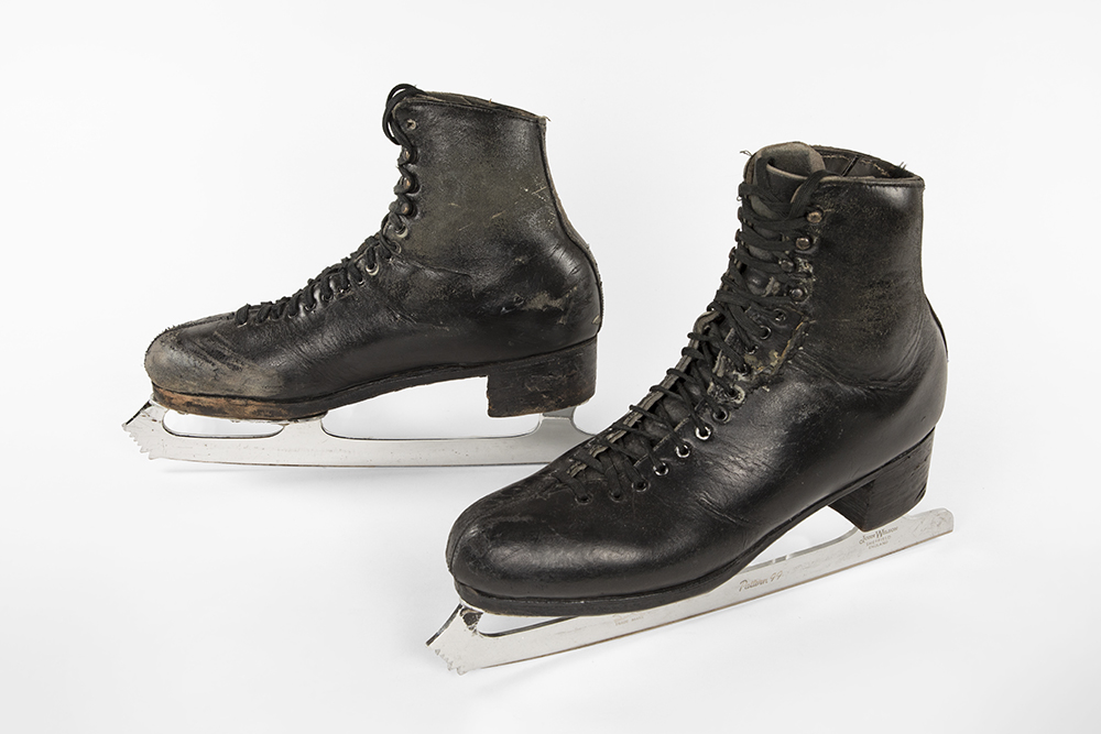 Photo of a male’s black pair of well worn leather lace-up skates placed side by side.