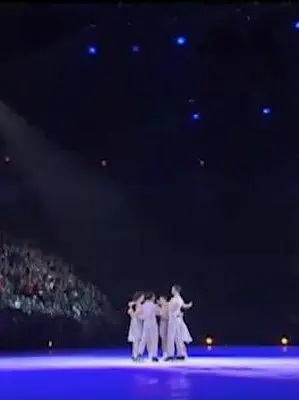 The seven skaters together at centre ice. The spotlights create a blue hue on the ice with the skaters highlighted in a yellow hue.