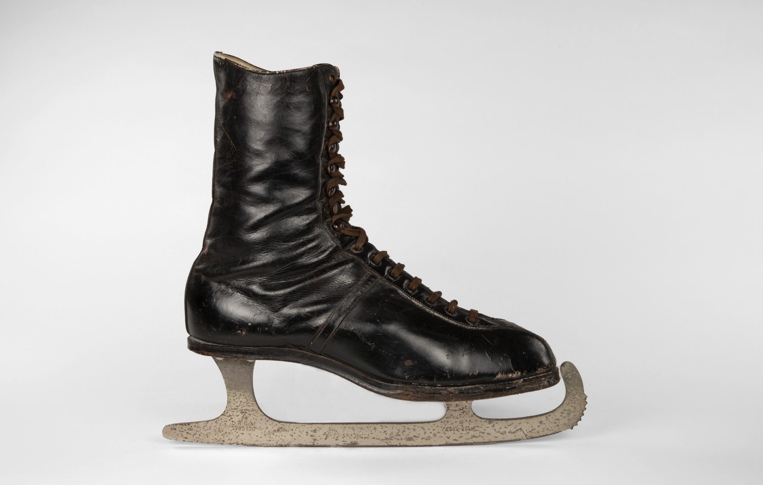 A profile view of a black leather boot with dark brown laces and a silver blade attached to the boot sole (with unseen screws). 