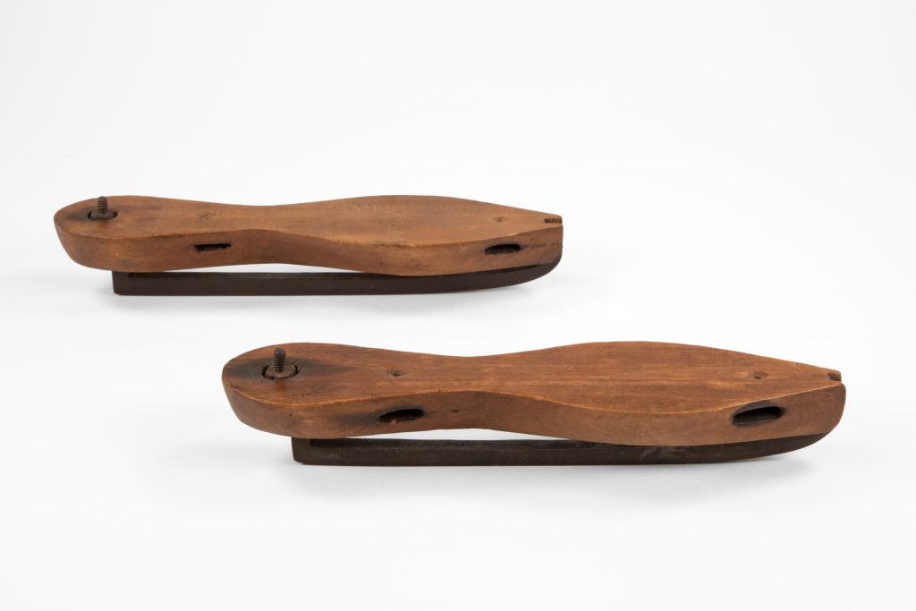 Paire de lames de patins, vues toutes deux de profil, montrant la section médiane étroite de la semelle, qui donne sa forme de violon à la plateforme où repose le pied.