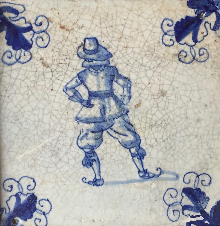 Tuile blanche avec l’illustration, en bleu, d’un homme vu de dos qui patine. Chaque coin de la tuile est décoré d’une feuille bleue. 