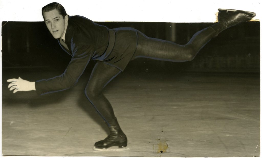 A black and white photo of McCreath on the ice, skating towards the left with his upper body bent forward, his bent left arm forward and left leg extended back, bent slightly at the knee. He wears a belted blazer, collared shirt and tie, and black knit tights.