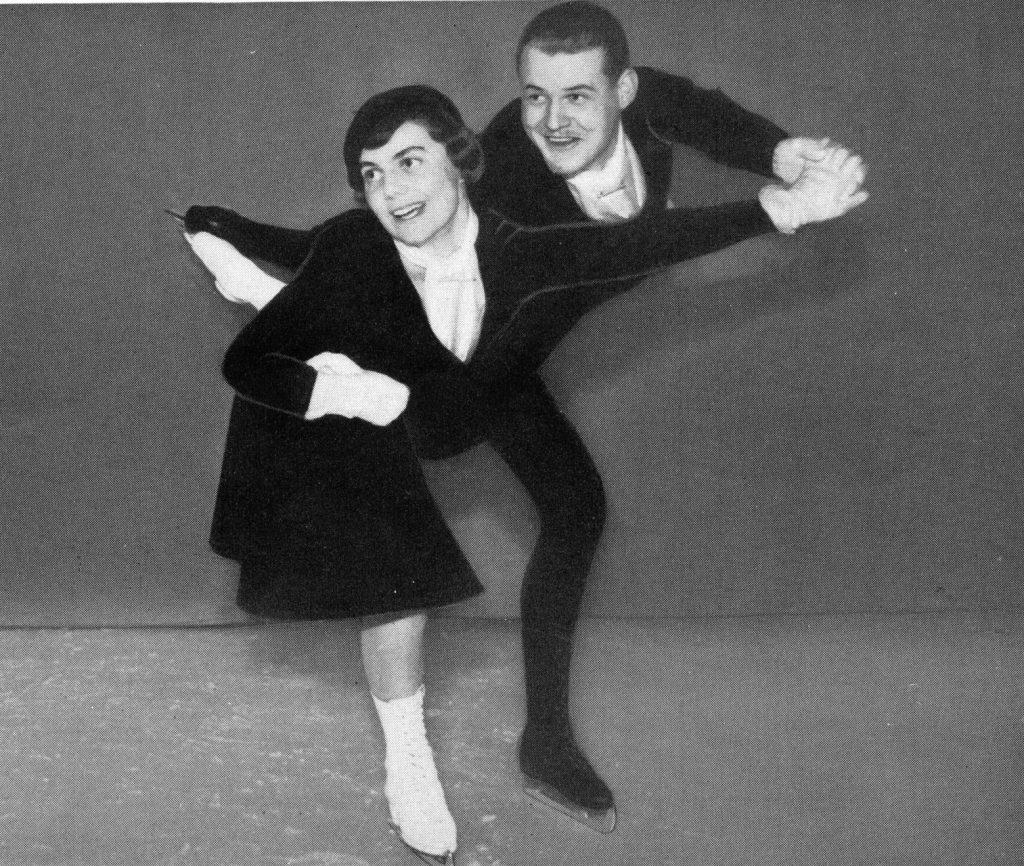 A black and white photo of a smiling man and woman skating towards the viewer. Their skating knees in front are bent and their left legs are extended to the back. She has white skates; he has black.
