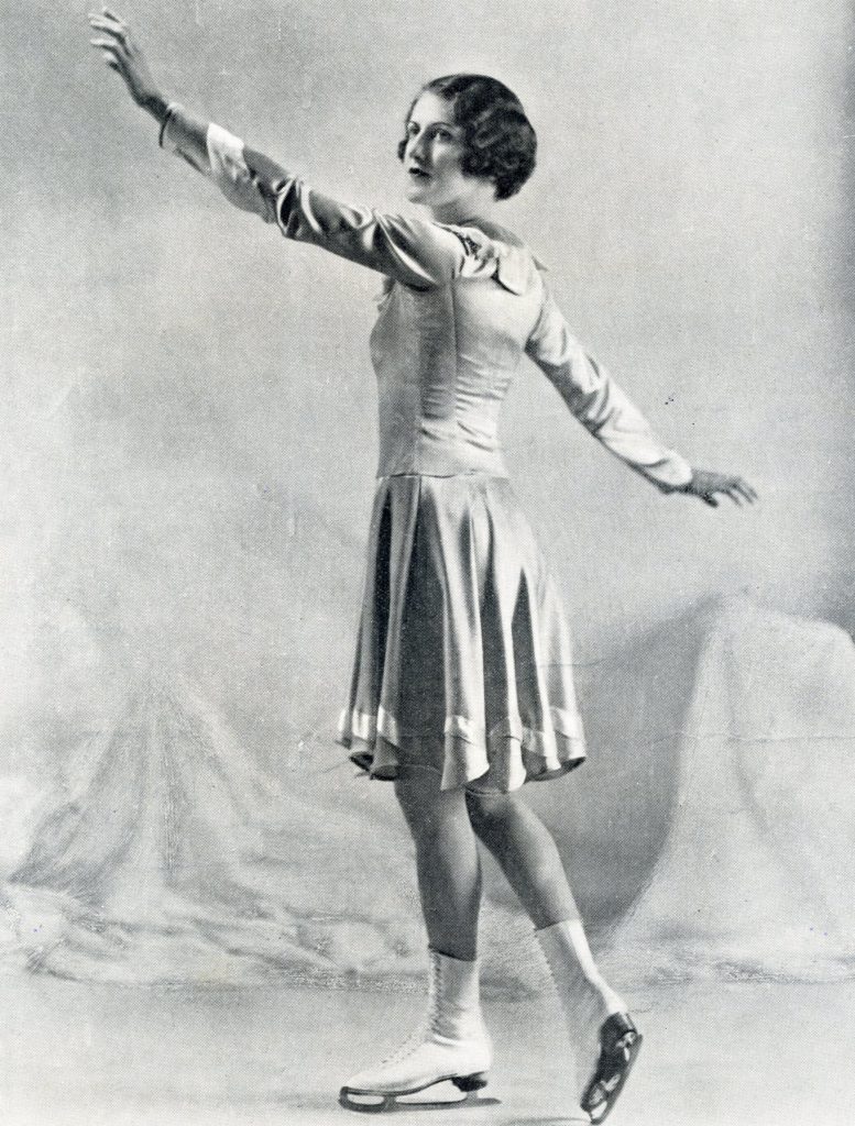 A black and white photo of a woman posing in skates, wearing a knee length, long sleeve skating dress. She faces the side.