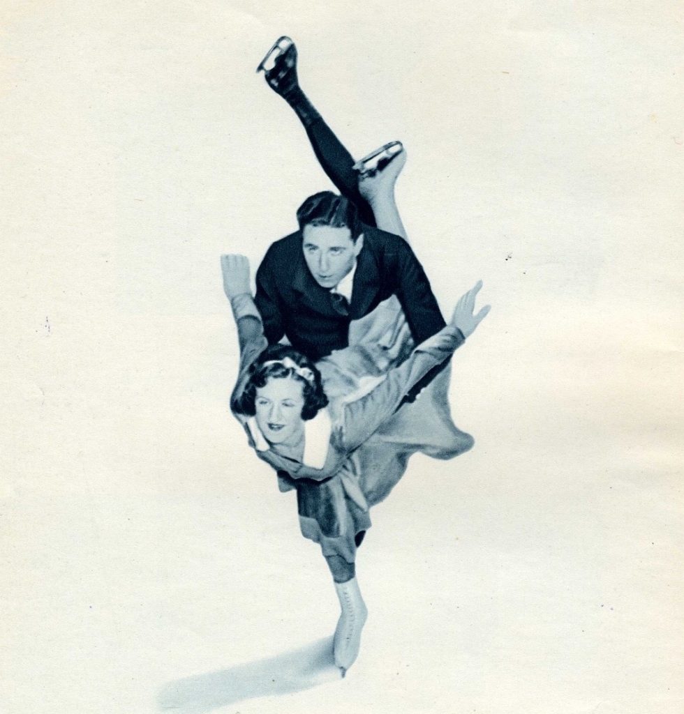 A black and white photo of a man and a woman skating towards the viewer, each with a leg extended. He holds her; her arms are extended behind her.