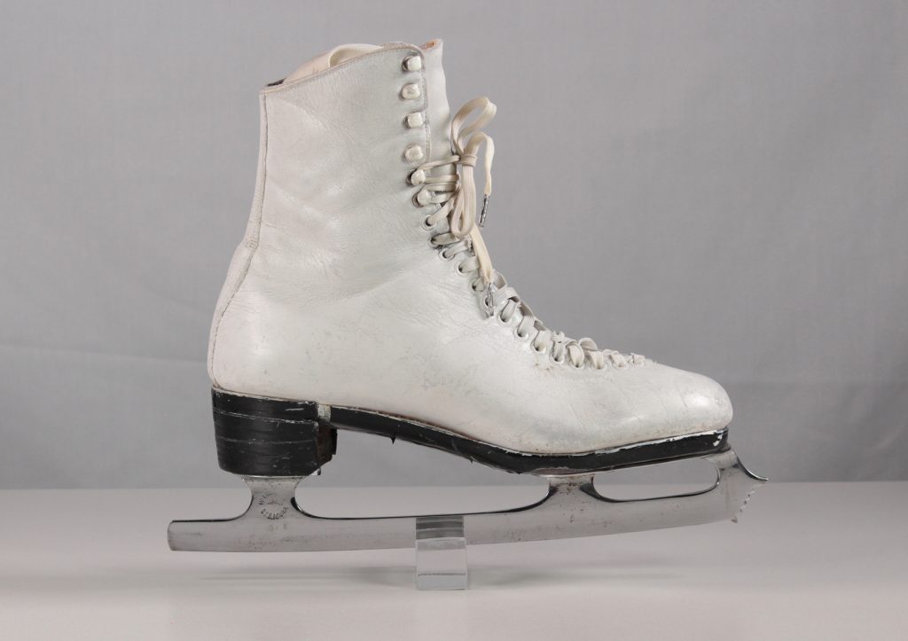 A colour photo of a single white skate in profile view. The stacked block heel has been covered neatly with black electrical tape.