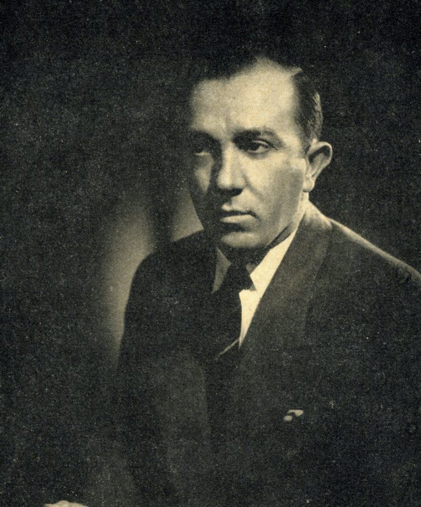 A black and white photo of a middle aged man in a suit and tie, shot from the waist up.