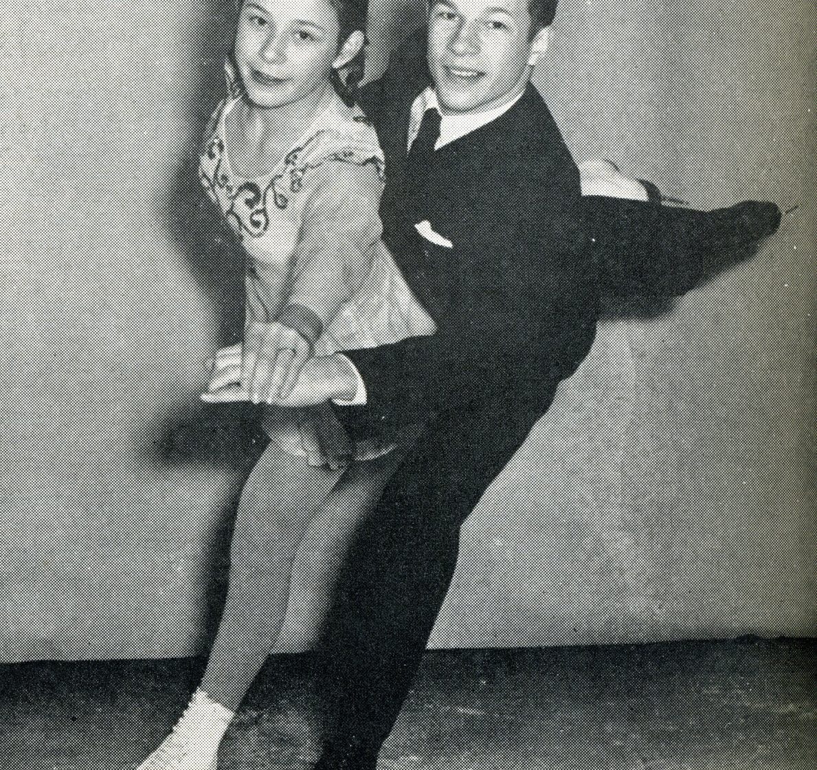 Photo rapprochée en noir et blanc d’un jeune homme et d’une jeune femme qui patinent ensemble vers les spectateurs, leurs mains jointes tendues devant eux.