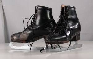 Pair of black men’s skates with blades attached. The boots are very worn at the toe on the inner side. The boot uppers are almost glossy with sheen.