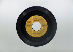 Photo of a black record disk with yellow gold label in the centre with text: “H.H. Bloom Sound Enterprises, Ottawa, Canada. This is a copy of the Customer’s tape. Speed 45 RPM.”