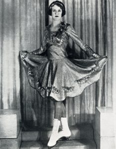 A black and white image of Constance Wilson-Samuel in a shimmery skating dress with very full knee-length skirt.