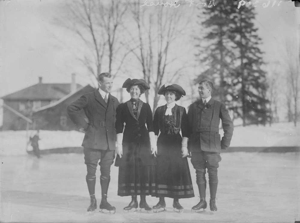 Une photo en noir et blanc de deux hommes et deux femmes, portant des patins et souriant à la caméra.