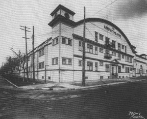 A black and white photo of a white multi-story building with many windows. Large lettering on the front of the building reads “The Amphitheatre”.