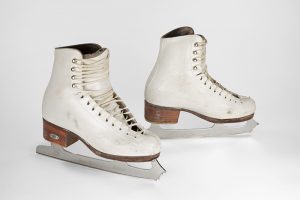 Photo of a pair of well-used white leather laced-up skates in three-quarter view.
